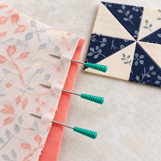 Illustrative use: green patchwork pins holding two fabric edges aligned before sewing. Pin diameter varies by listing.