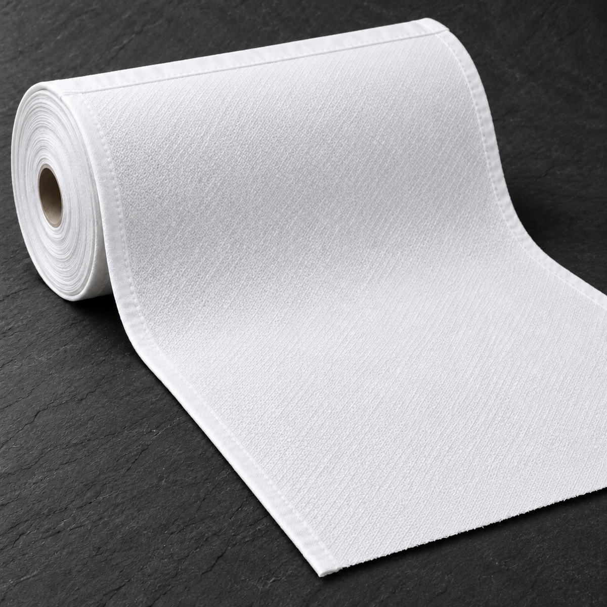 White huck fabric unrolling on a charcoal background, with a fine diamond weave, hemmed sides and a raw cut end